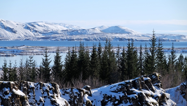 Paysage nordique enneigé fait d'un lac, avec des sapins devant et des montagnes dans le fond.