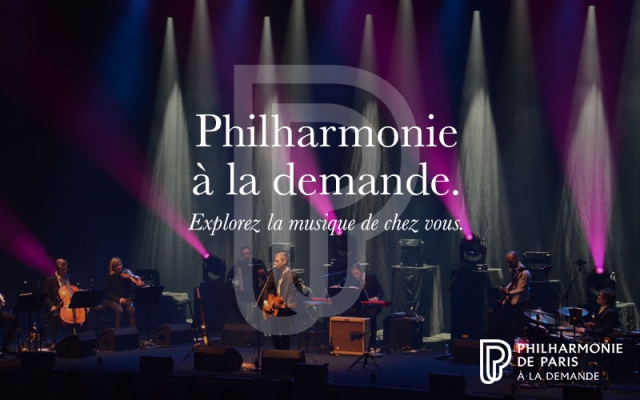 Orchestre sur scène avec éclairage violet. Il est écrit au centre par dessus l'image : Philharmonie à la demande, explorez la musique de chez vous + logo en bas à droite.